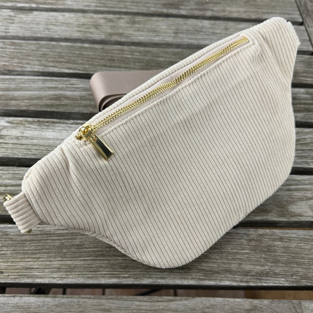 MAONI Bauchtasche in der Farbe Taupe auf einer hölzernen Tischoberfläche, mit sichtbarem und sicherem Reißverschlussfach auf der Rückseite.