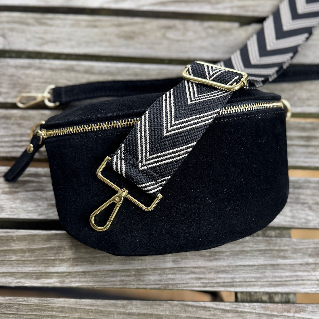 Schwarze Veloursleder Bauchtasche mit goldenem Verschluss liegt auf Tisch