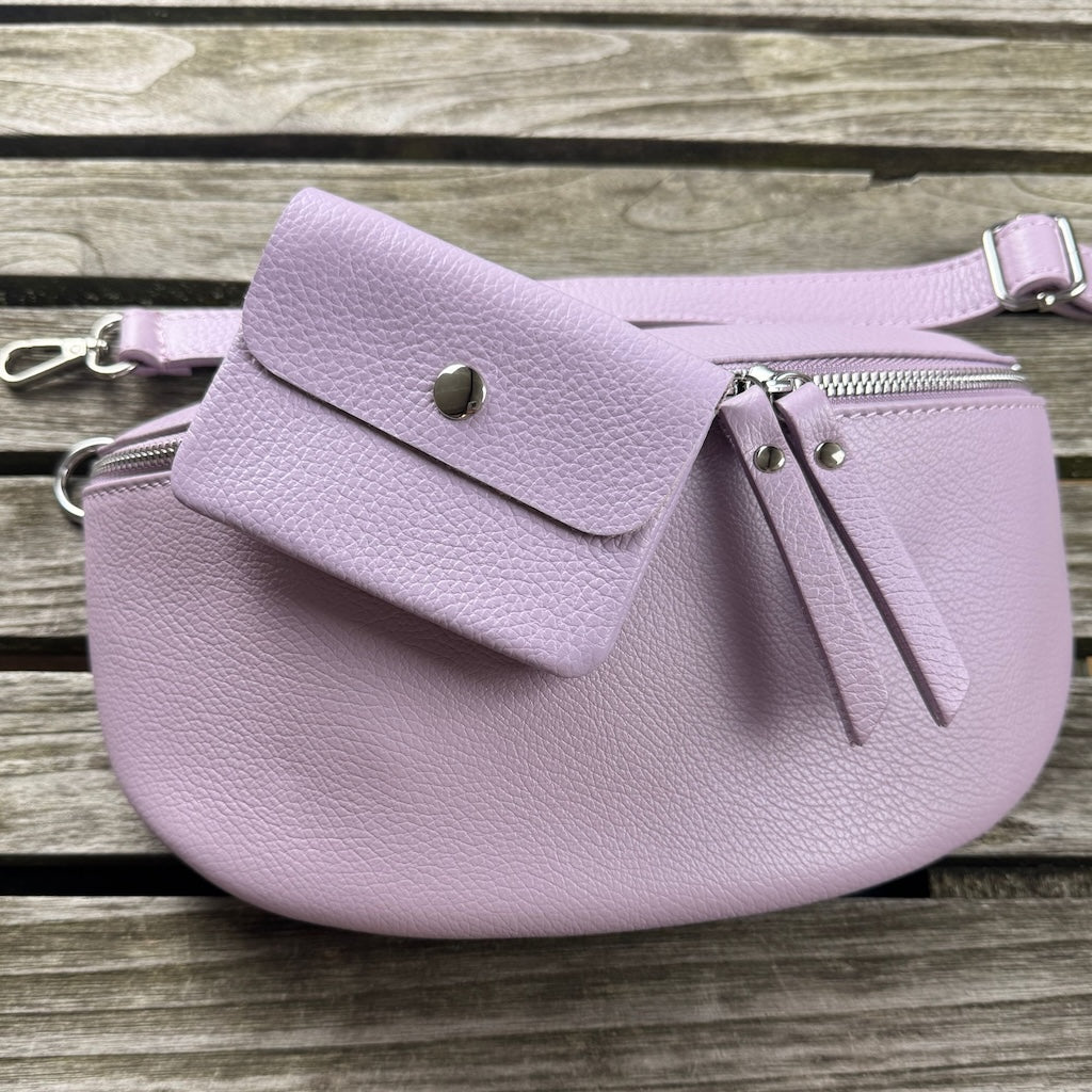 MAONI-Bauchtasche in Lila liegt auf Holztisch, darauf liegt die farblich passende Geldbörse aus Leder