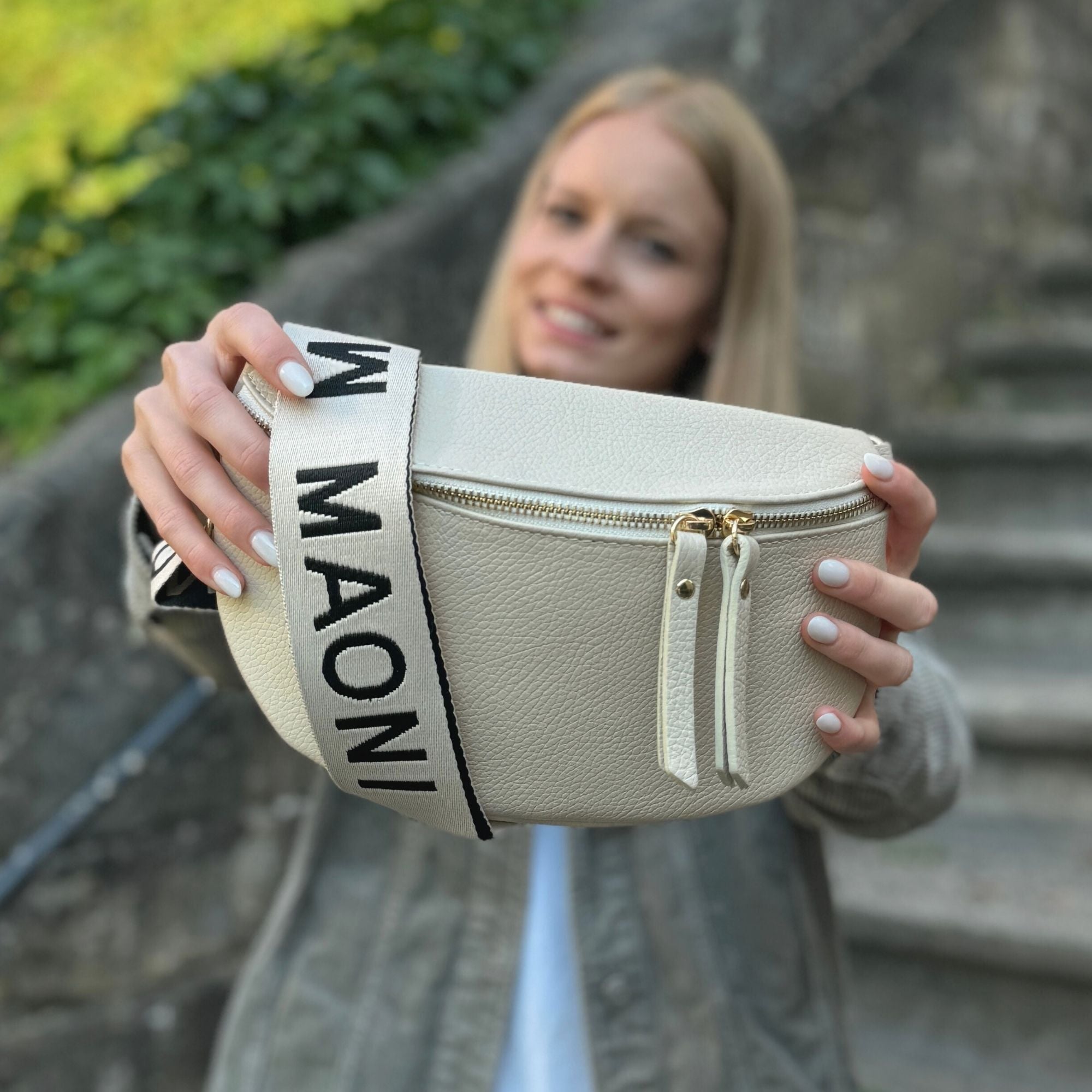 Frau hält Beige Lederbauchtasche mit Zwei Wege Reißverschluss und MAONI Taschengurt in den Vordergrund.