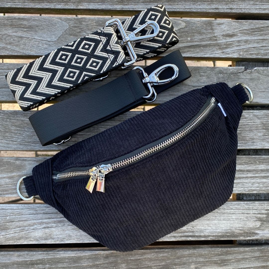 Schwarze Cord-Bauchtasche mit auswechselbarem Gurt (Muster: gezackt) und Reißverschluss auf der Rückseite – praktisch und stylisch.