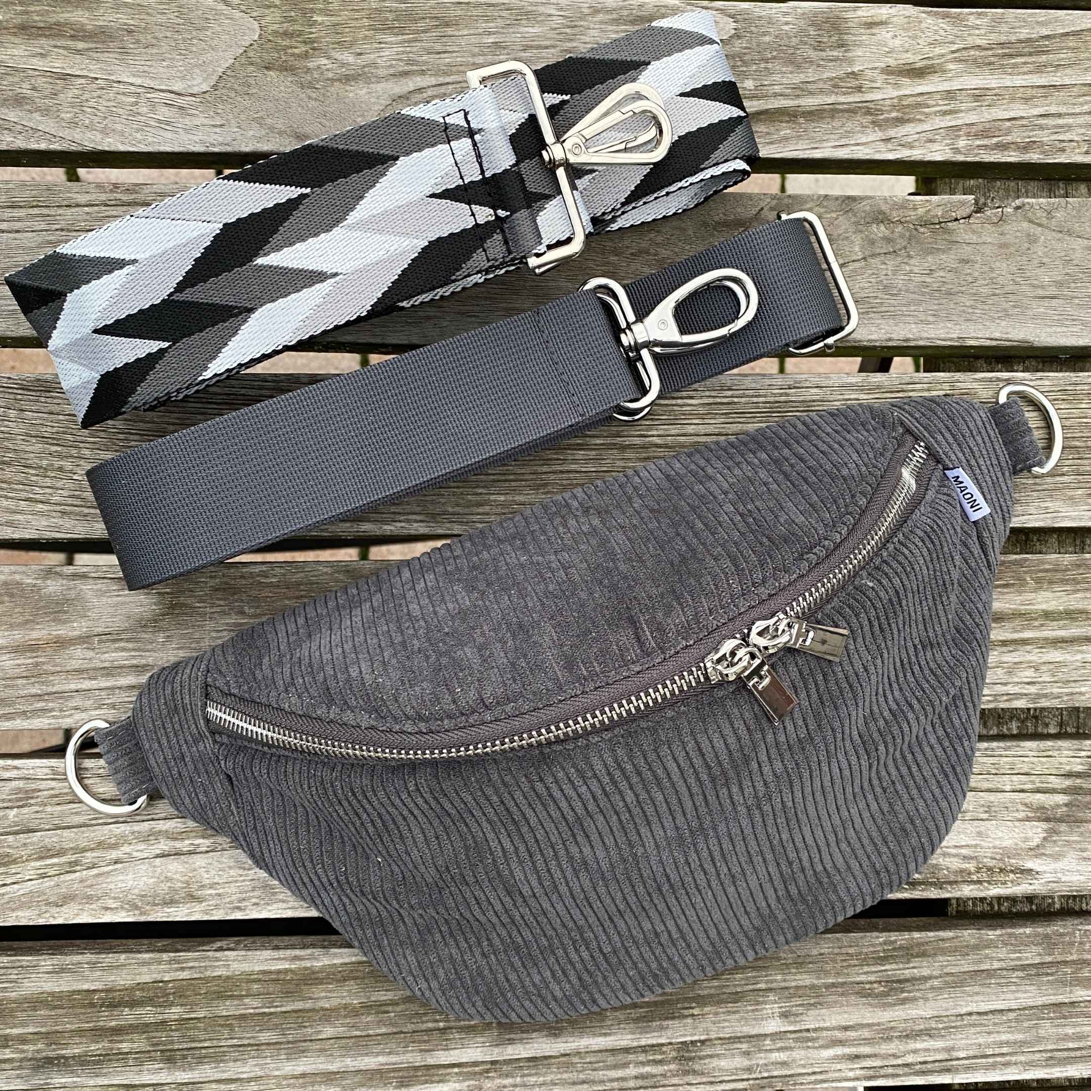 Graue Bauchtasche aus Cord mit verstellbarem, auswechselbarem Gurt in den Farben schwarz-grau und sicherem Reißverschlussfach auf der Rückseite.
