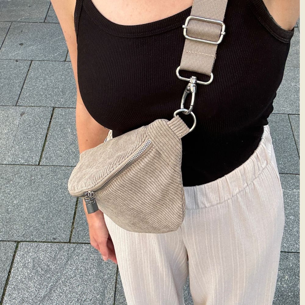 Cord-Bauchtasche mit einfarbigem grünen Gurt, der gewechselt werden kann. Getragen von einer jungen Frau mit lockerem Outfit.