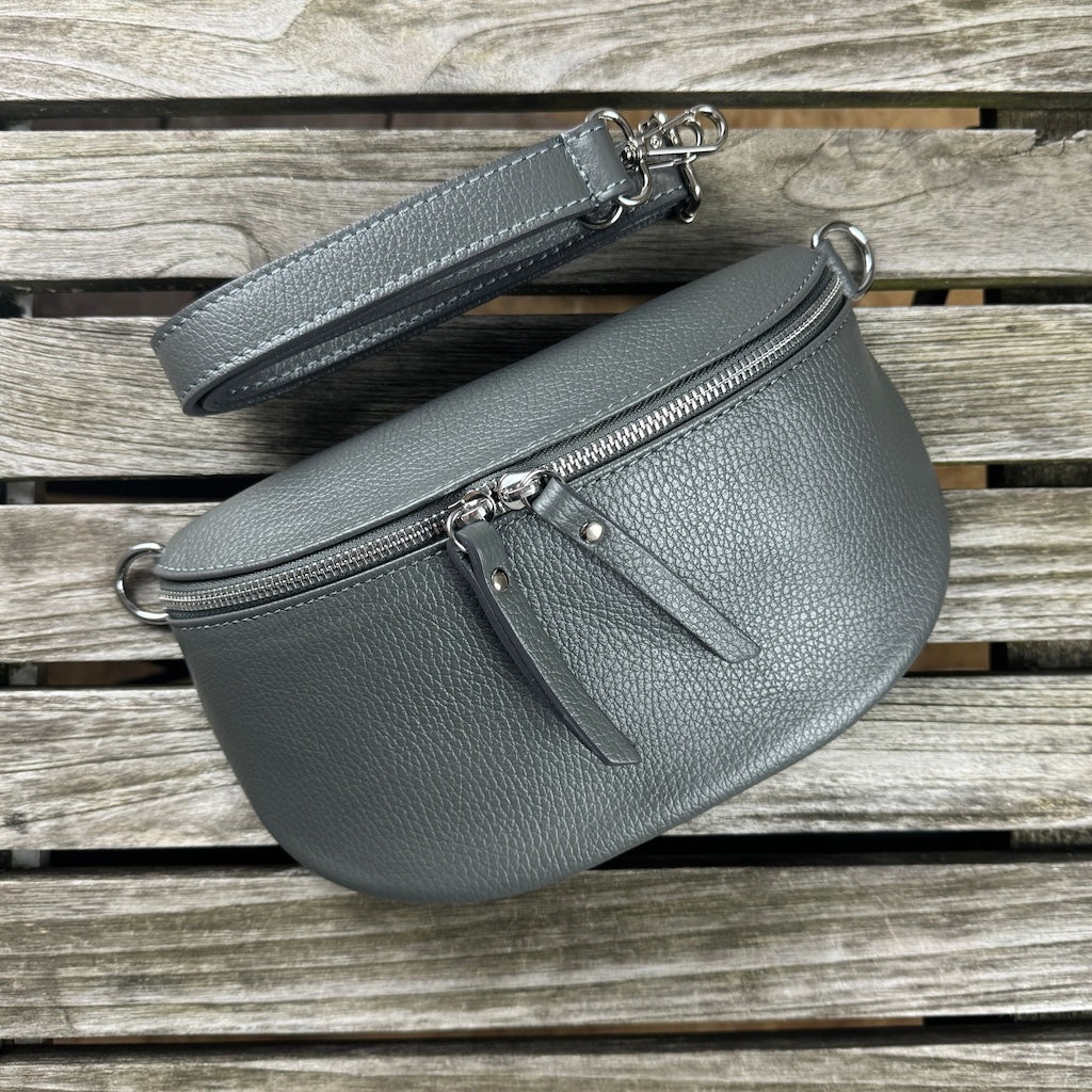 Dunkelgraue Bauchtasche aus Leder liegt auf Holztisch. Der Taschengurt ist auswechselbar.