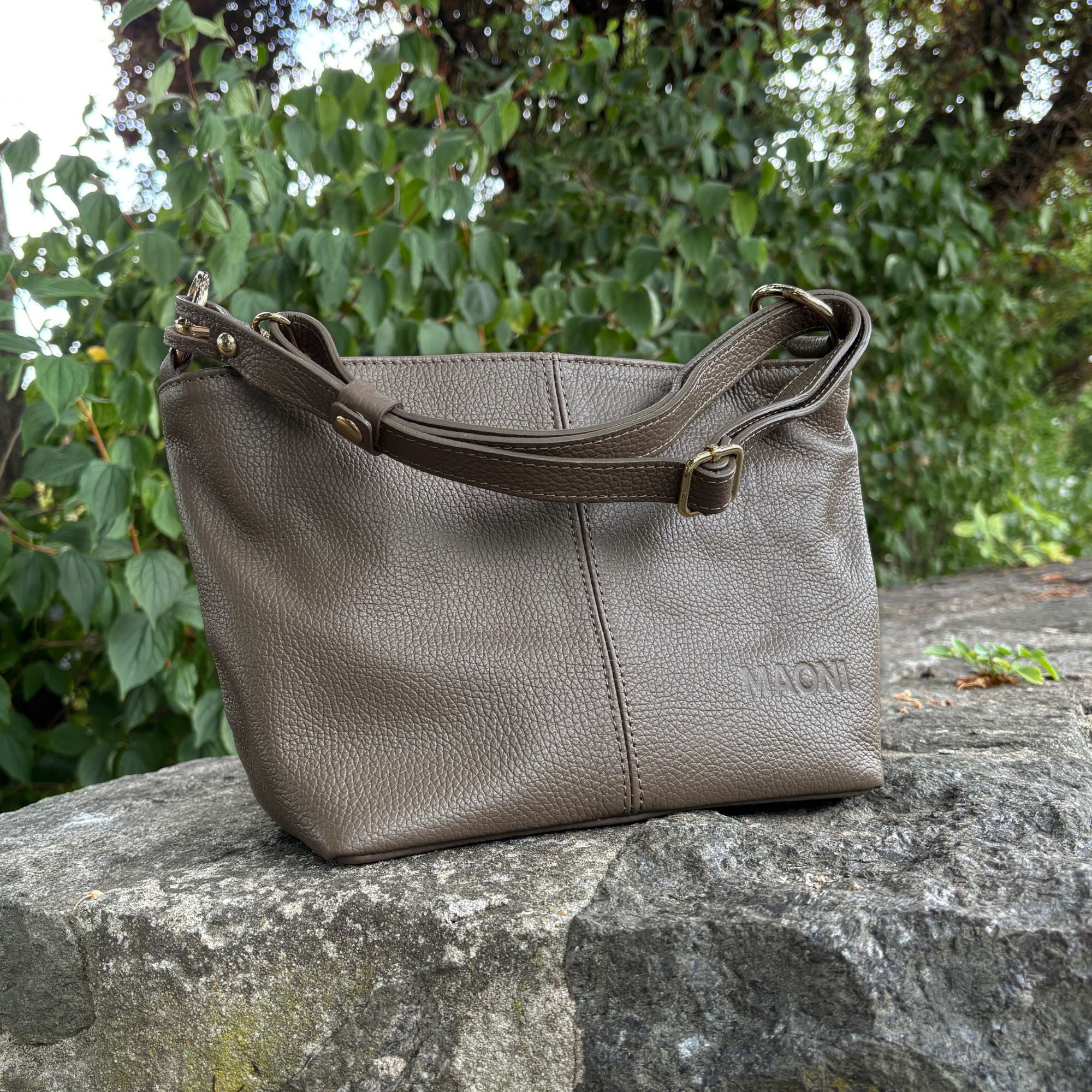 Umhängetasche Monica in Dunkeltaupe aus Leder auf einem Stein