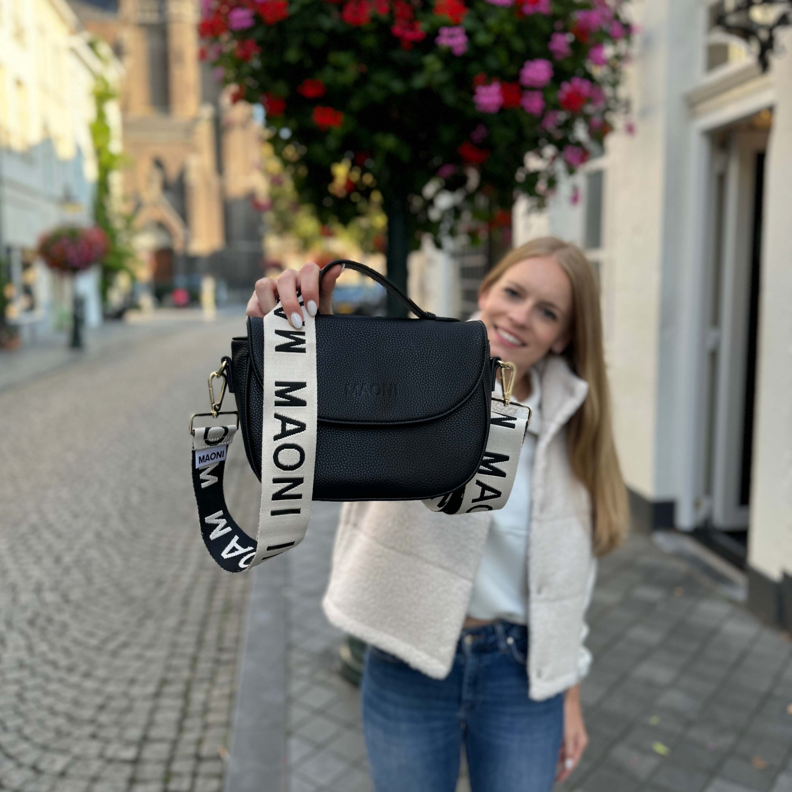 Modische Half Moon Bag wird von Frau im Vordergrund gehalten, während sie im Hintergrund fröhlich lacht. Die Tasche ist in der Farbe Schwarz gehalten.