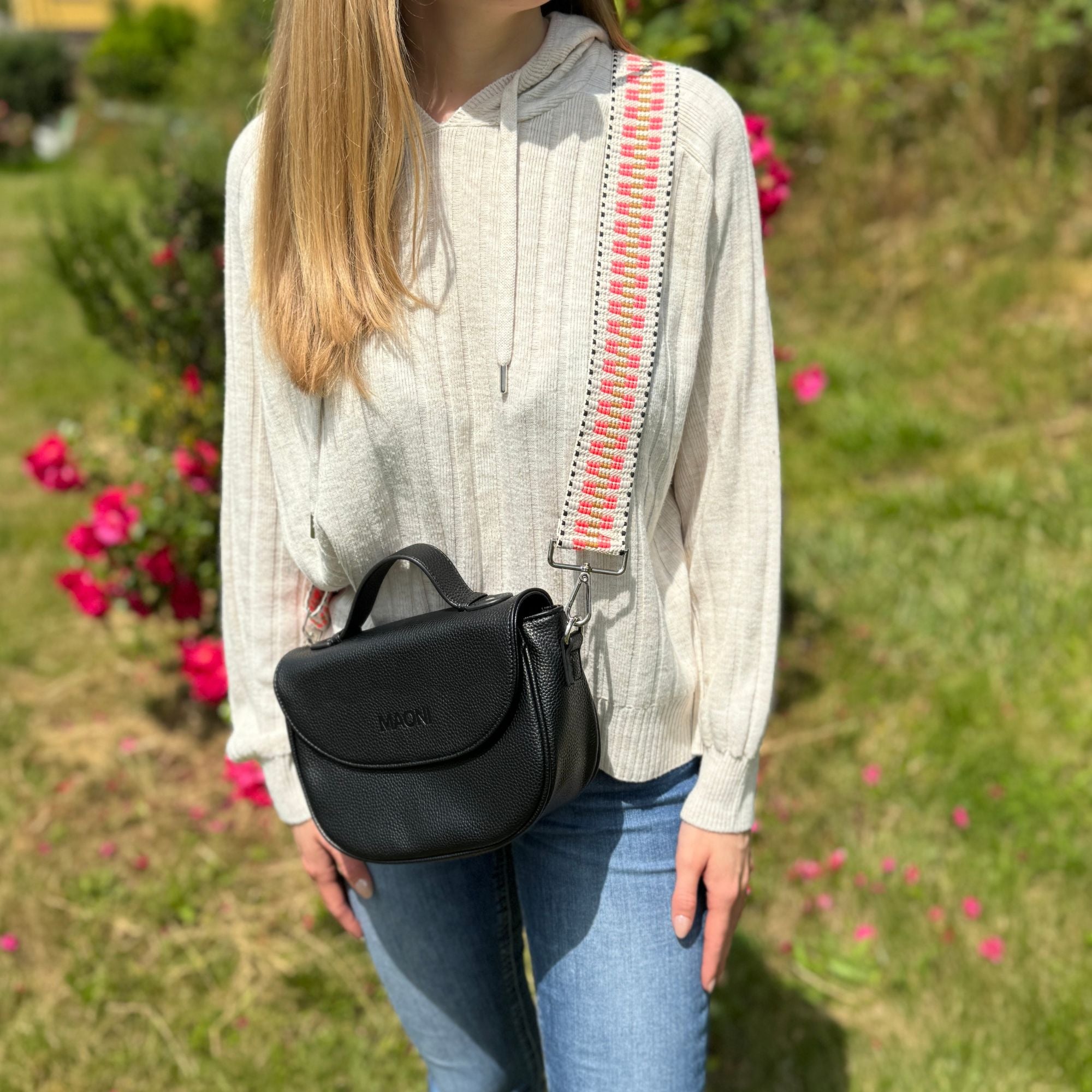 Frau trägt schwarze Halfmoon-Tasche in der Natur, kombiniert mit einem auffälligen neon-pinken Gurt.