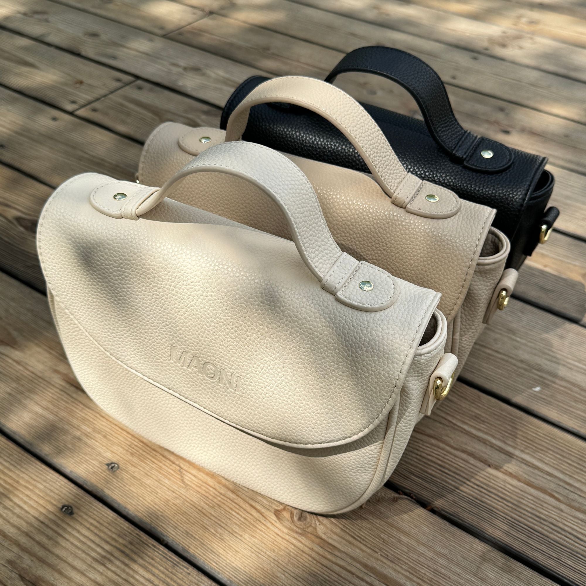 Halfmoon Taschen stehen hintereinander. Von vorne nach hinten: Beige, Taupe, Schwarz.