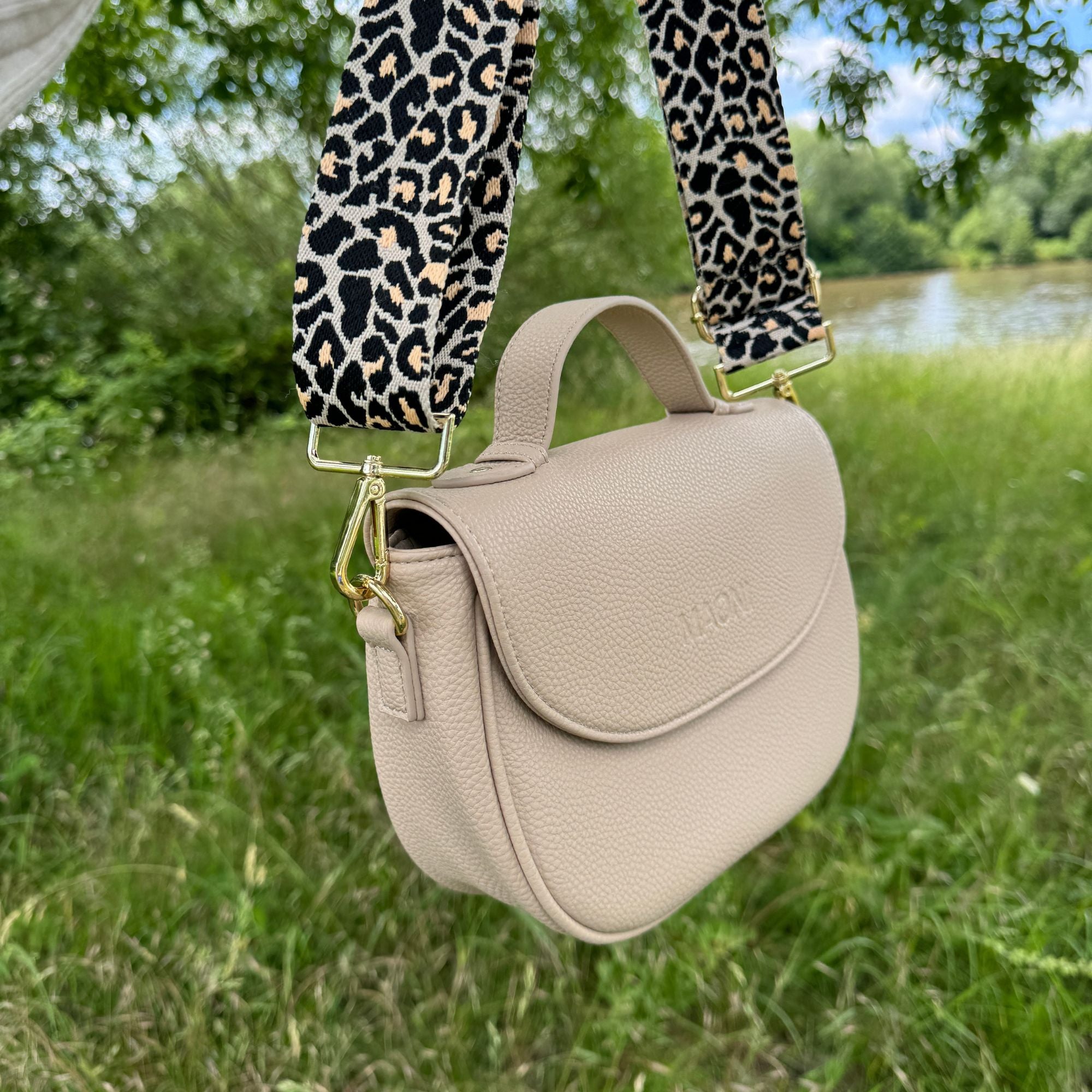 Taupefarbene Halfmoon-Tasche mit Leo-Gurt hängt in der Natur – stilvolles Accessoire im natürlichen Umfeld.