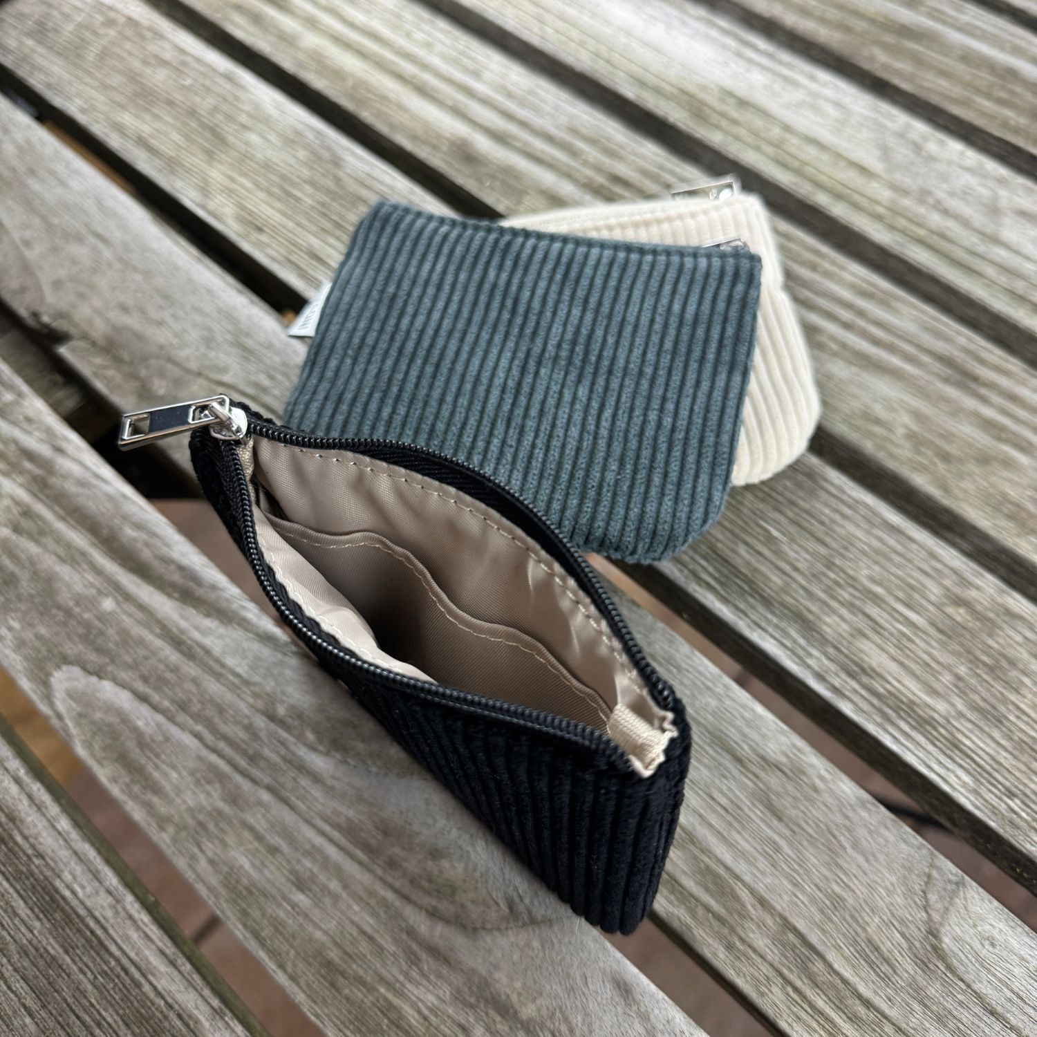 Cord Etuis in dunkelgrau, beige und schwarz im Hintergrund – stilvolles Trio auf einem rustikalen Holztisch.