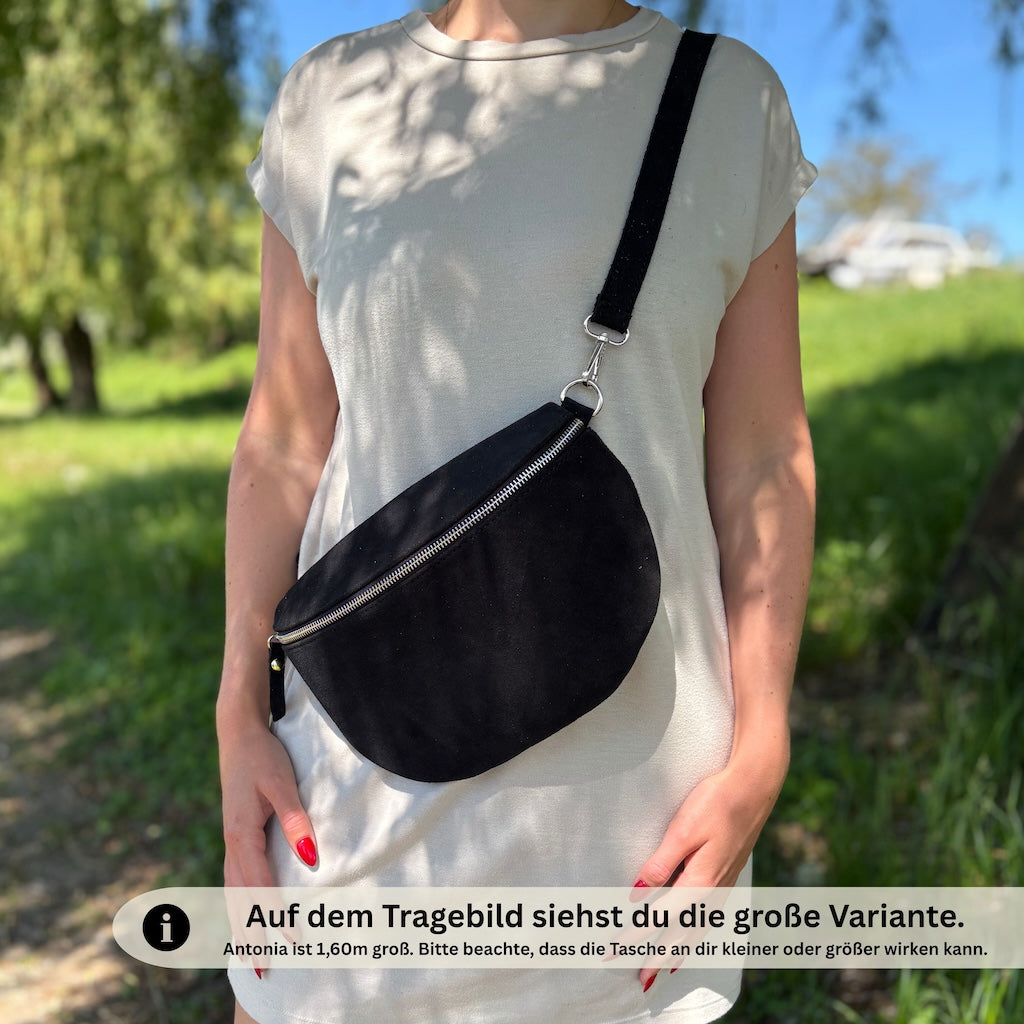 Schwarze Bauchtasche aus Veloursleder getragen von Frau mit beigen Kleid.