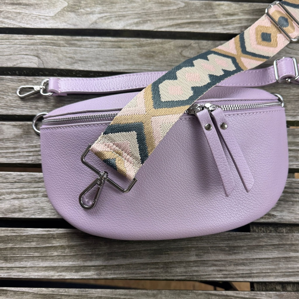 Variantenbild auf Holz: MAONI-Bauchtasche in Lila, dazu schmaler Leder- und breiter Muster-Gurt in den Farben grau, braun, rosa im Flatlay