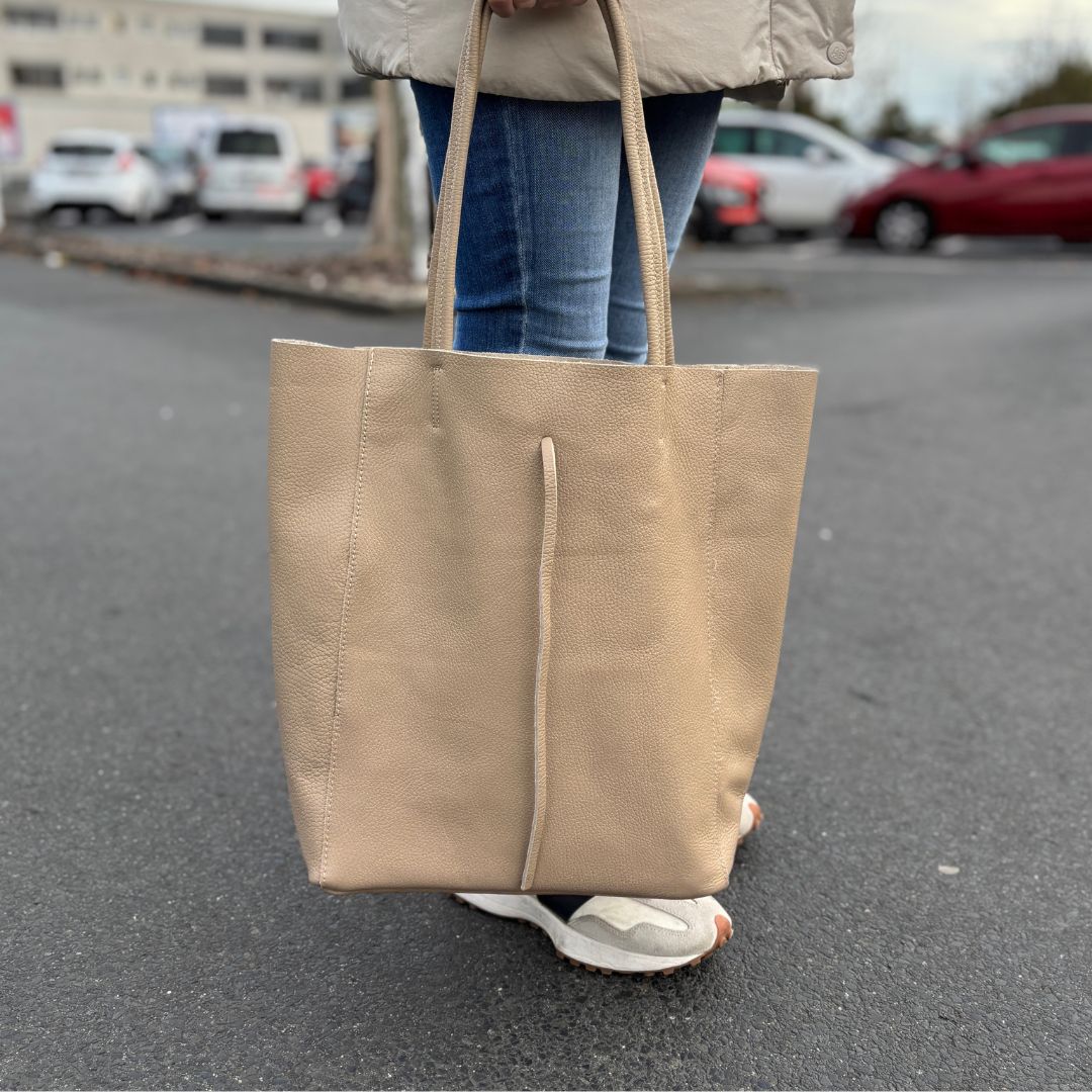 Taupefarbener Leder-Shopper, getragen von einer Frau auf einem Parkplatz – praktisch und gleichzeitig elegant.