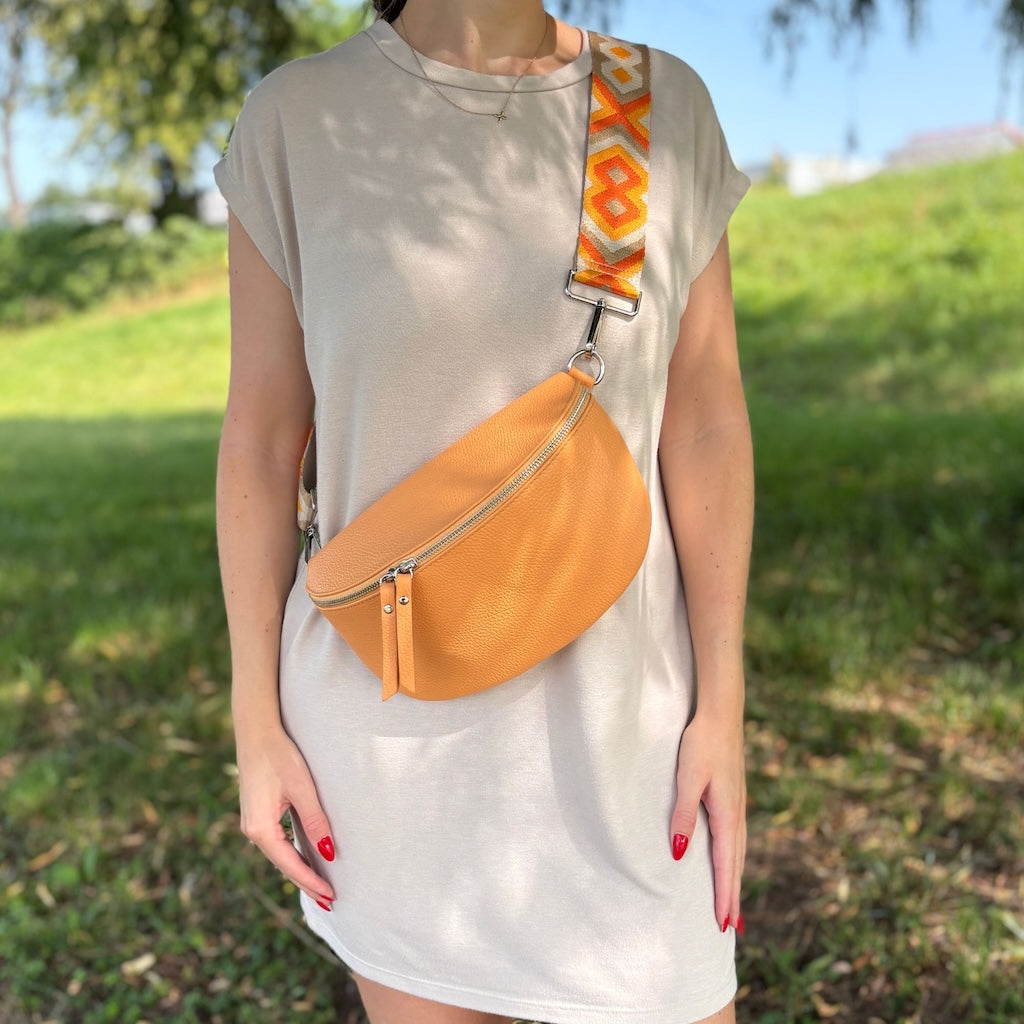 Frau trägt Bauchtasche in Pfirsich-Farbton mit breitem gemustertem Gurt – farbenfroher Sommerlook, getragen im Alltag