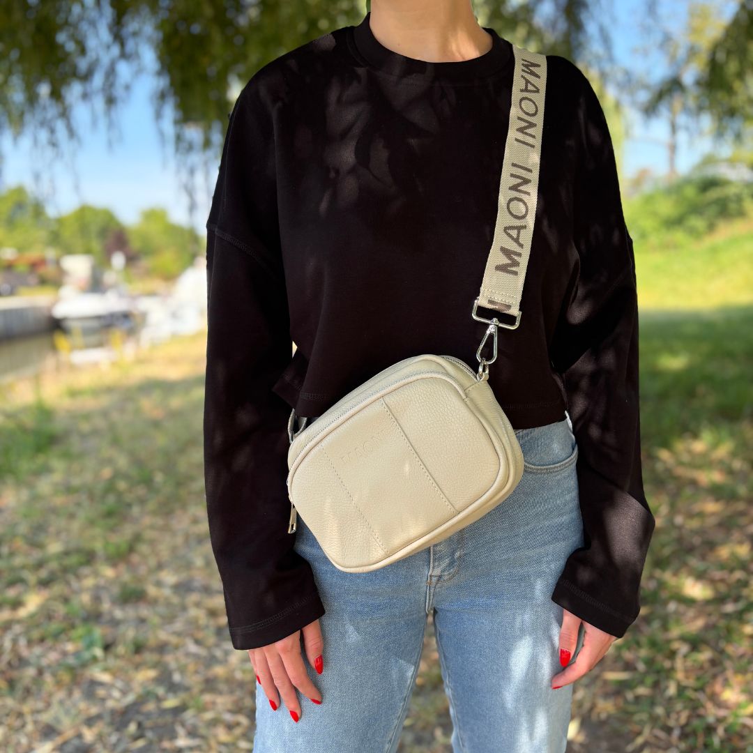 Beige Crossbody-Tasche mit MAONI Logo Schultergurt, von einer Frau lässig im Bootshafen Mainkur getragen