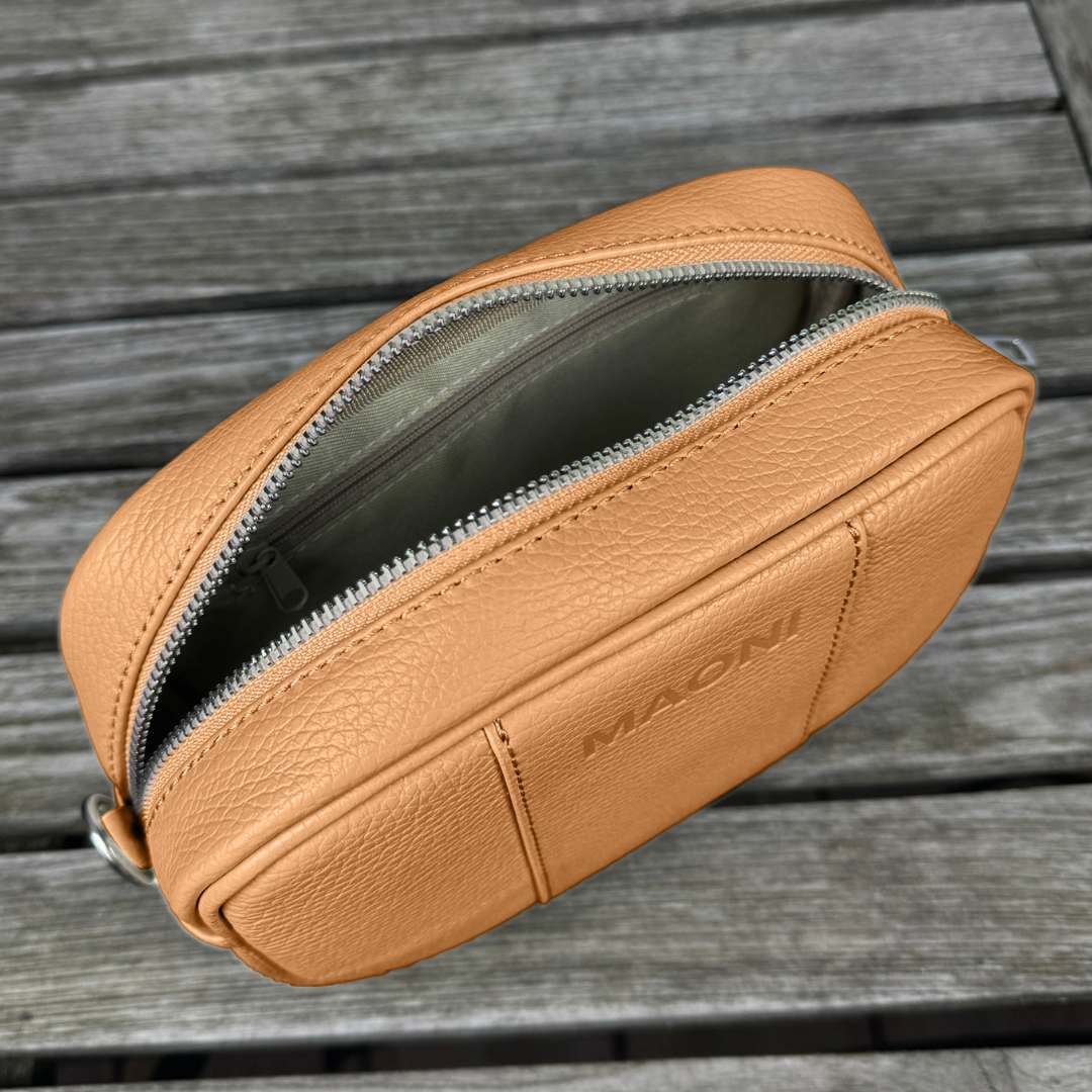Offene MAONI Crossbody-Tasche auf einem Tisch, zeigt Innenfächer mit Einsteckfach und Reißverschlussfach. Die Tasche hat die Farbe Cognac.