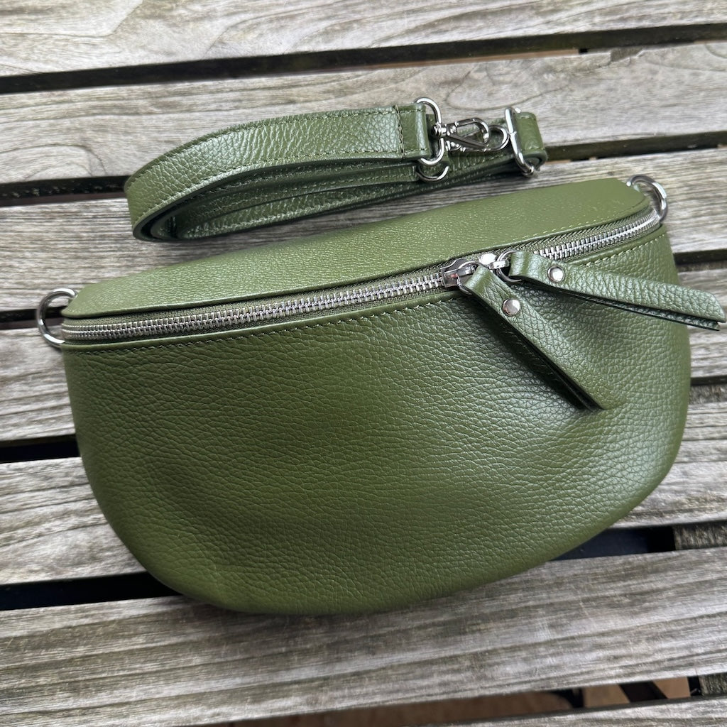 Große dunkelgrüne MAONI-Bauchtasche, flach mit Vorderseite nach oben auf Holztisch gelegt – schmaler Wechselgurt liegt darüber