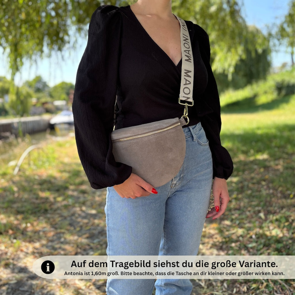 Stilvoller Naturlook: Frau trägt Bauchtasche aus dunkeltaupefarbenem Wildleder zu schwarzer Bluse beim Spaziergang am Sportboothafen Mainkur