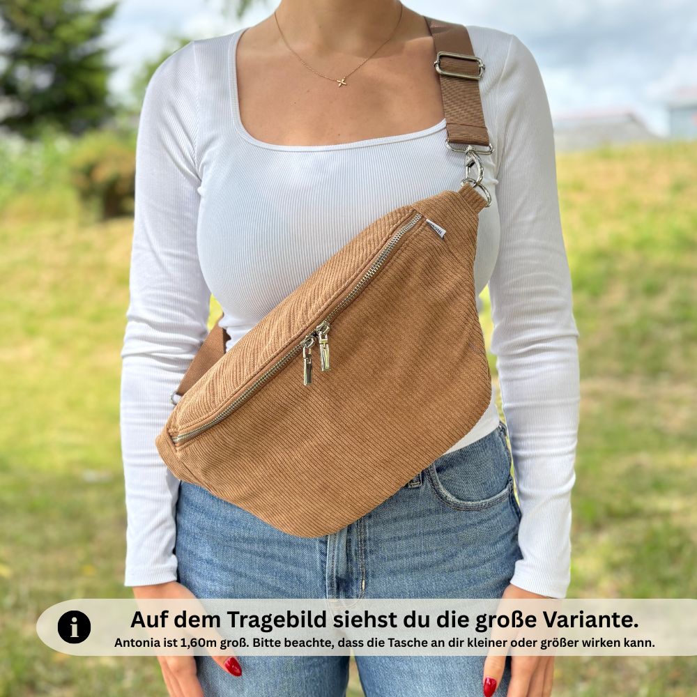 Große braune Bauchtasche aus Cord, lässig crossbody getragen von Frau mit weißem Oberteil und Jeans – Größenhinweis ‚Model 1,60 m‘ im Bild enthalten