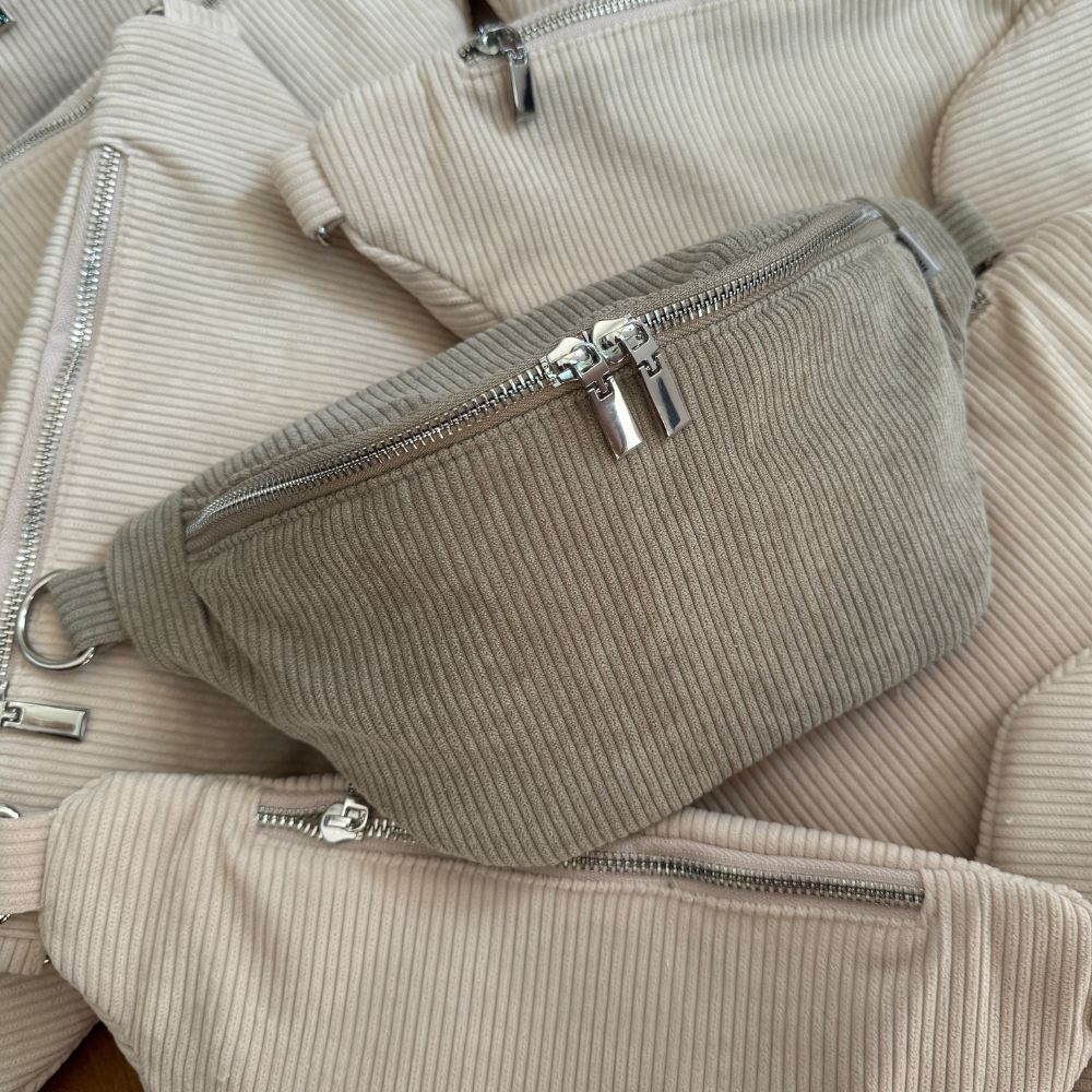 Cord Szene:  grüne Cord Bauchtasche liegt in einem Meer von beigen Cord Bauchtaschen.