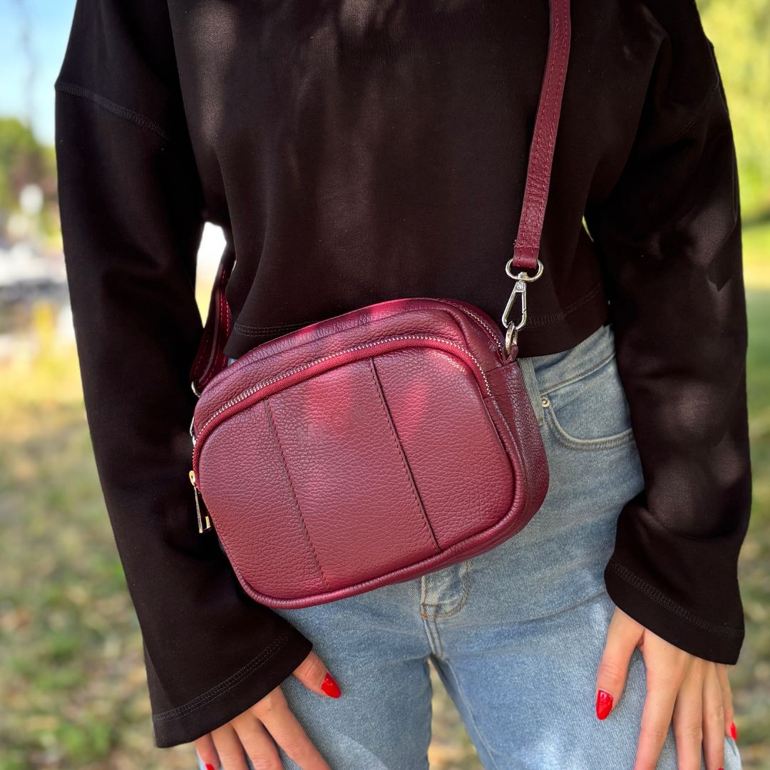 Burgunderrote Crossbody-Tasche mit breitem gemustertem Schultergurt, von einer Frau lässig crossbody getragen
