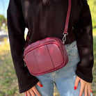 Burgunderrote Crossbody-Tasche mit breitem gemustertem Schultergurt, von einer Frau lässig crossbody getragen